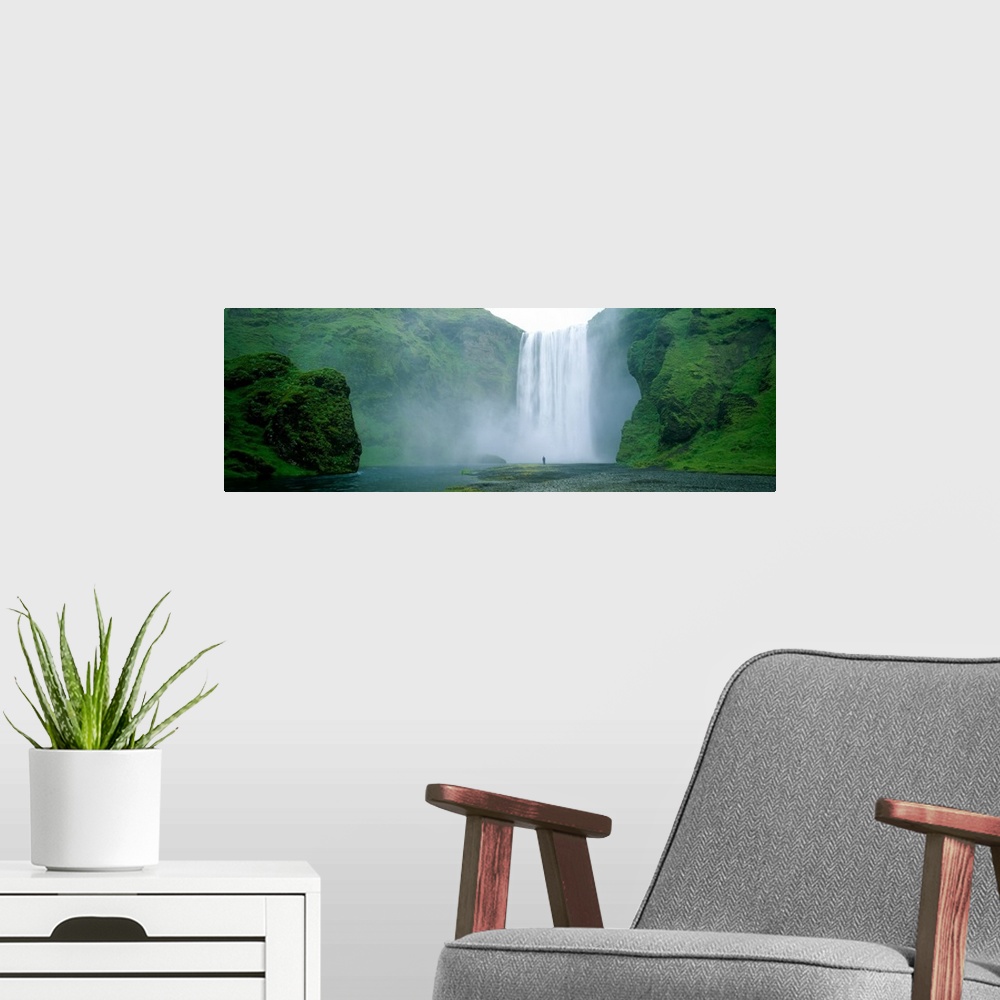 A modern room featuring Panoramic photo of a wide waterfall spilling over a cliff into the water below with a man standin...