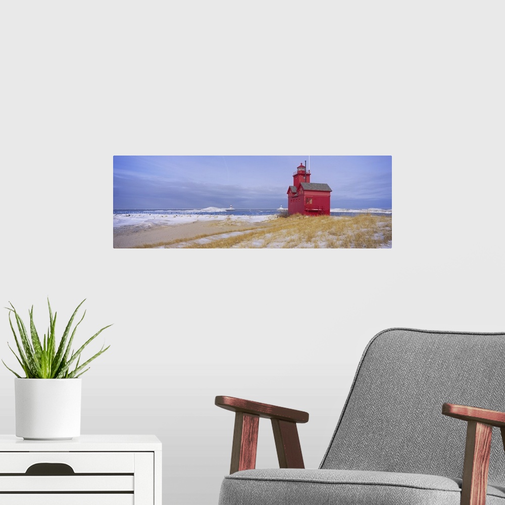A modern room featuring Lonely red light house on the edge of the water on a snowy beach, standing out against the pale c...