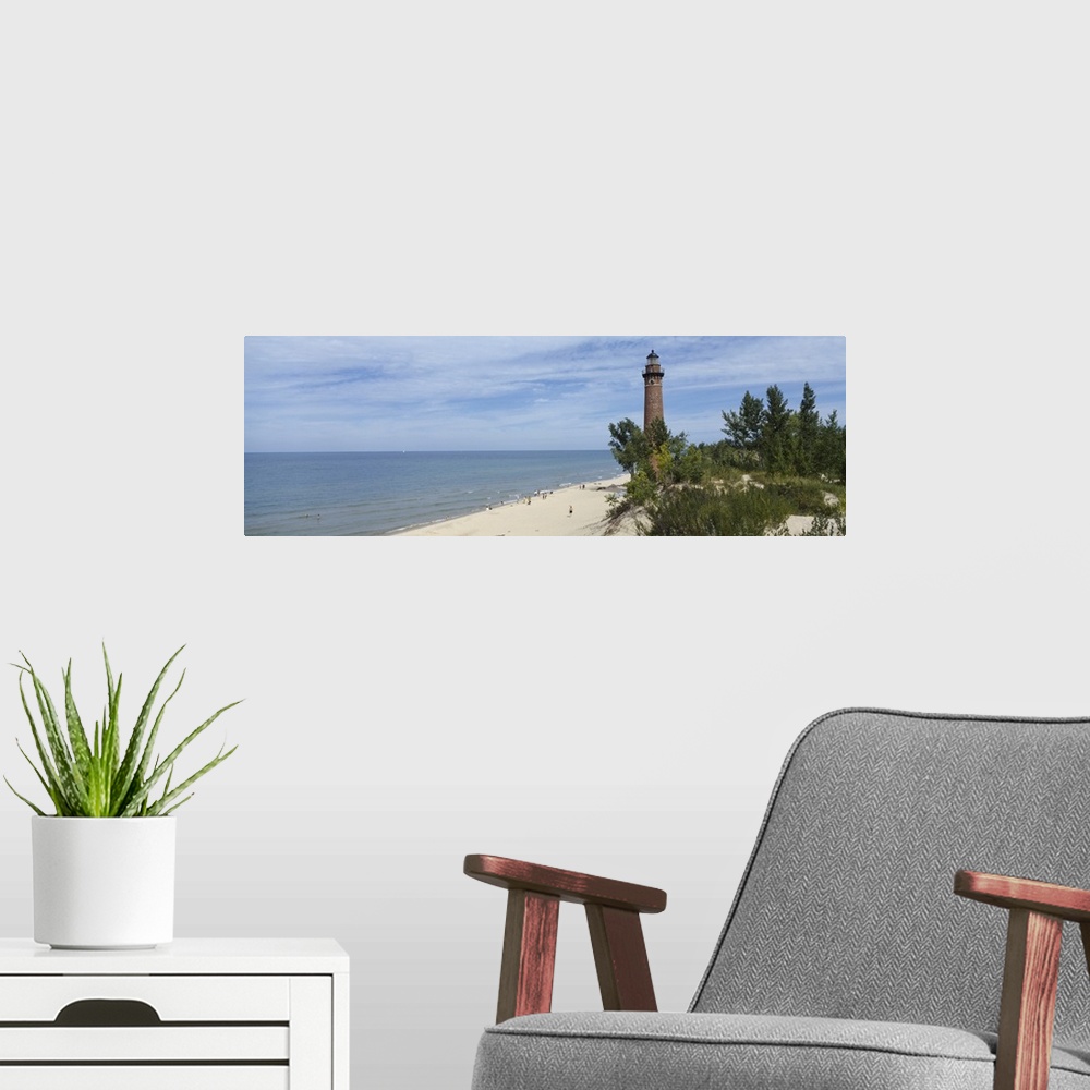 A modern room featuring A light house on a sandy shore obscured by costal plant life and a partially cloudy sky.