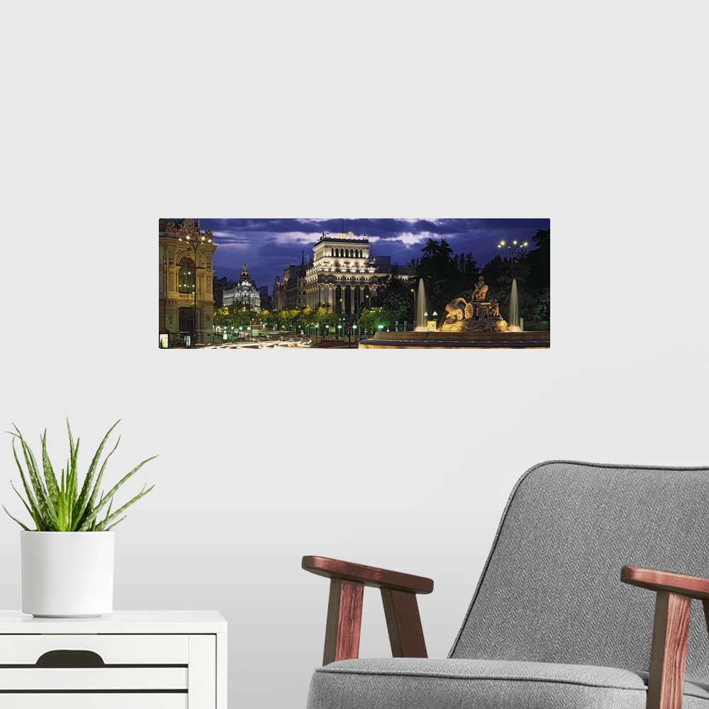 A modern room featuring Panoramic photo of old Spanish buildings around a traffic circle with long exposed car lights goi...