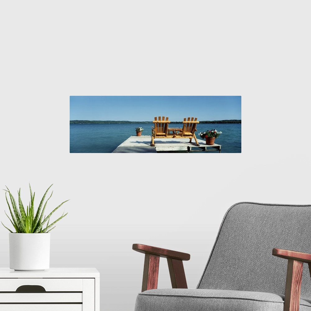 A modern room featuring This panoramic photograph is taken from behind two chairs sitting on a dock looking out over a bo...