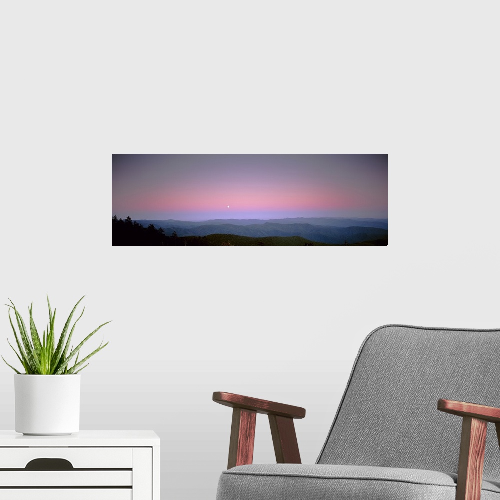 A modern room featuring Mountains in the distance are photographed under a sunset sky with a small view of the moon.