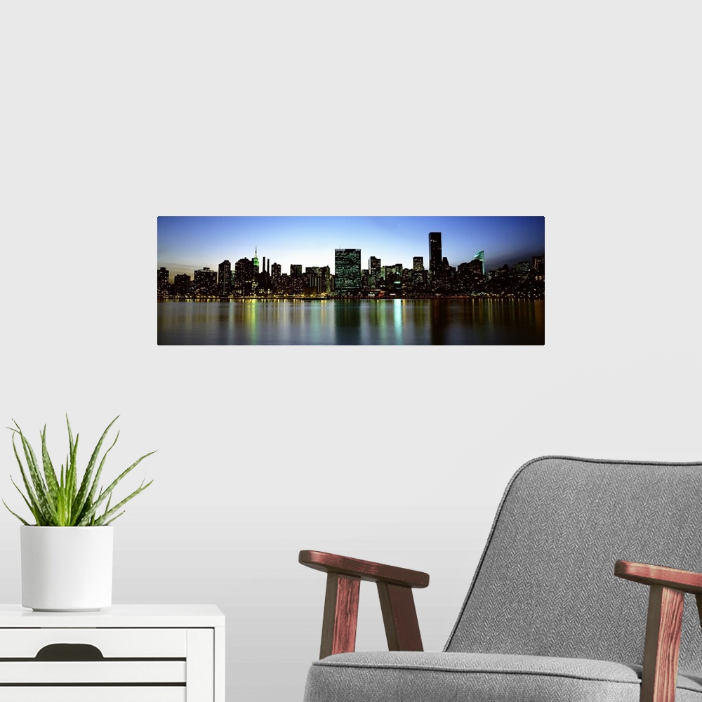 A modern room featuring Panoramic photograph of the New York City skyline, lit at dusk and reflecting in the waters in th...