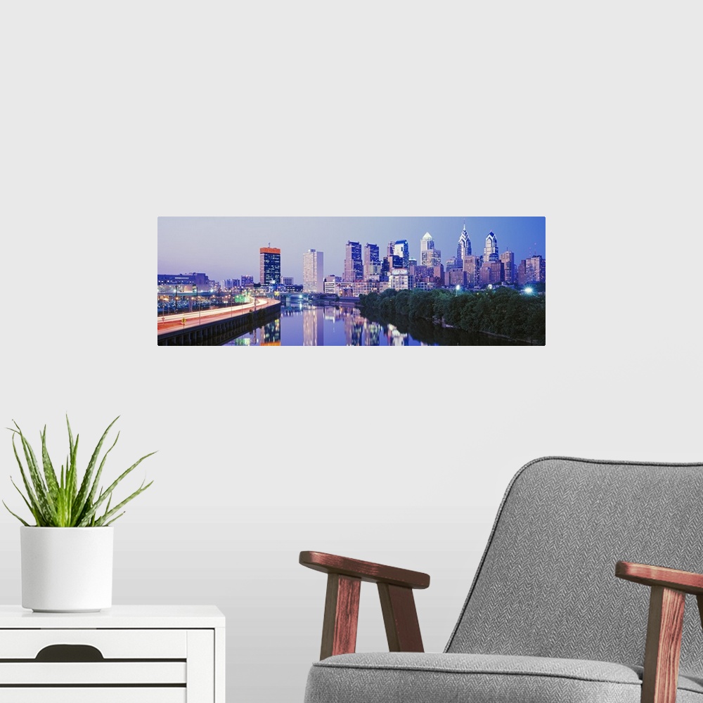 A modern room featuring This artwork is a panoramic canvas of the city skyline reflecting in the river water at dusk.