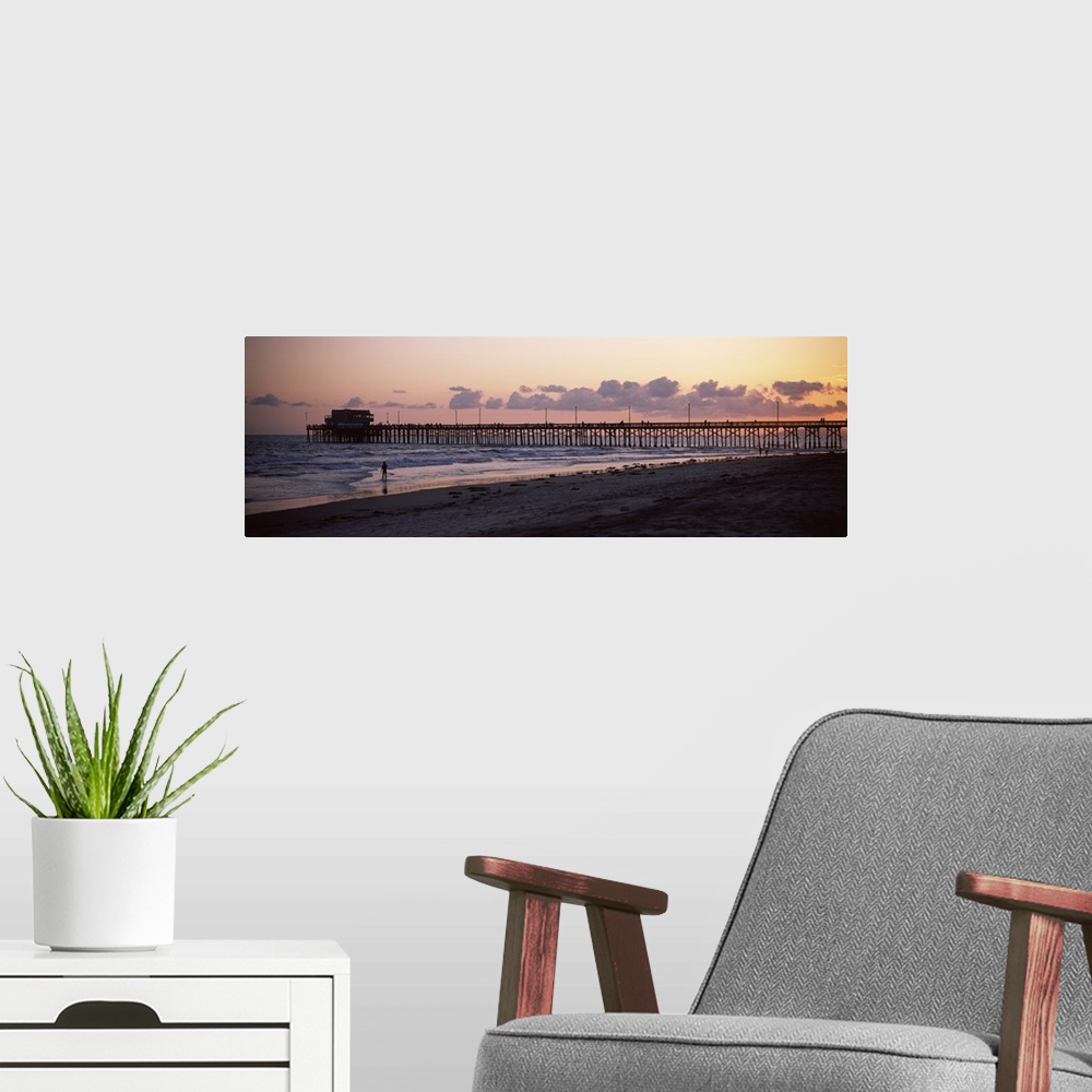 A modern room featuring A beach board walk extends out into the ocean in this landscape photograph of the sun setting on ...