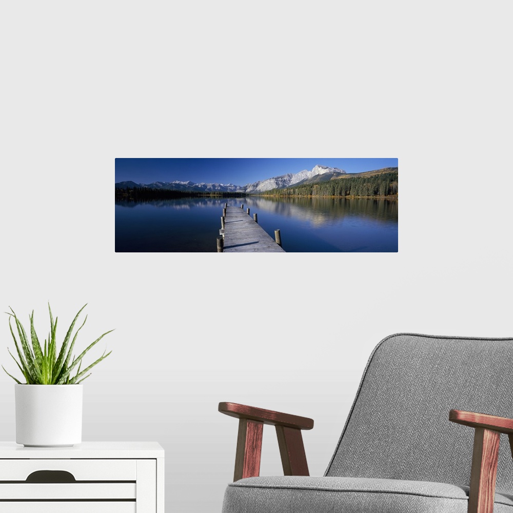 A modern room featuring Panoramic photograph of tilted wooden dock stretching into the water.  There is a forest line and...