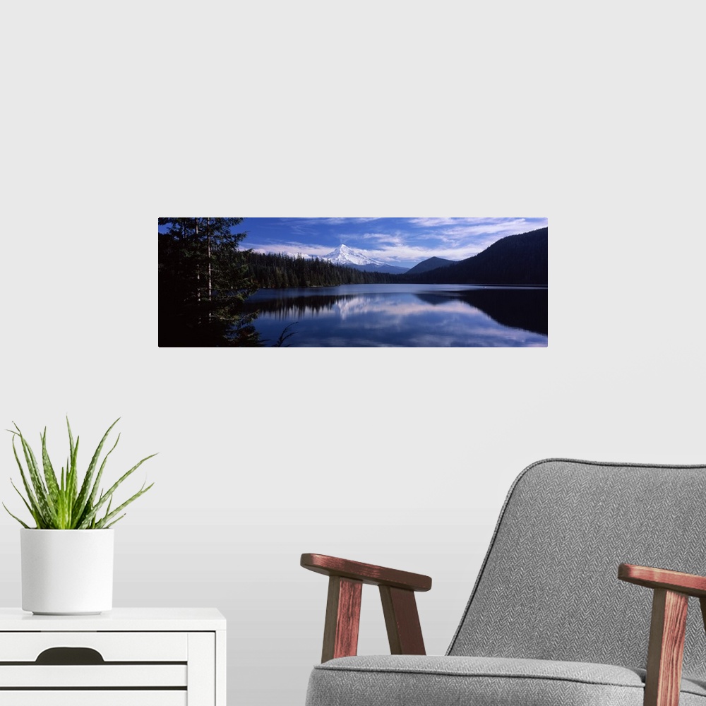 A modern room featuring A still lake photographed in wide angle view reflects a mountain that is seen just behind a thick...