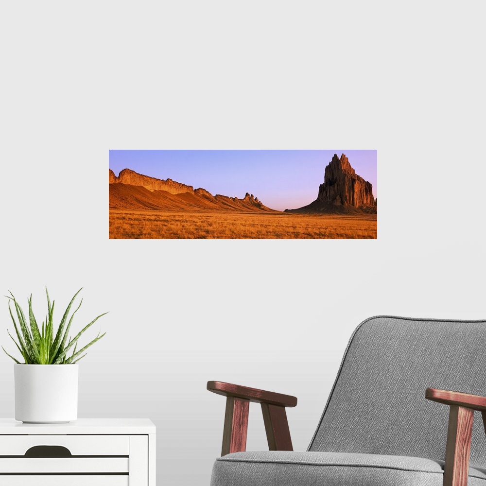A modern room featuring Ship Rock mountain is skewed to the right side of this panoramic piece with vast desert terrain t...