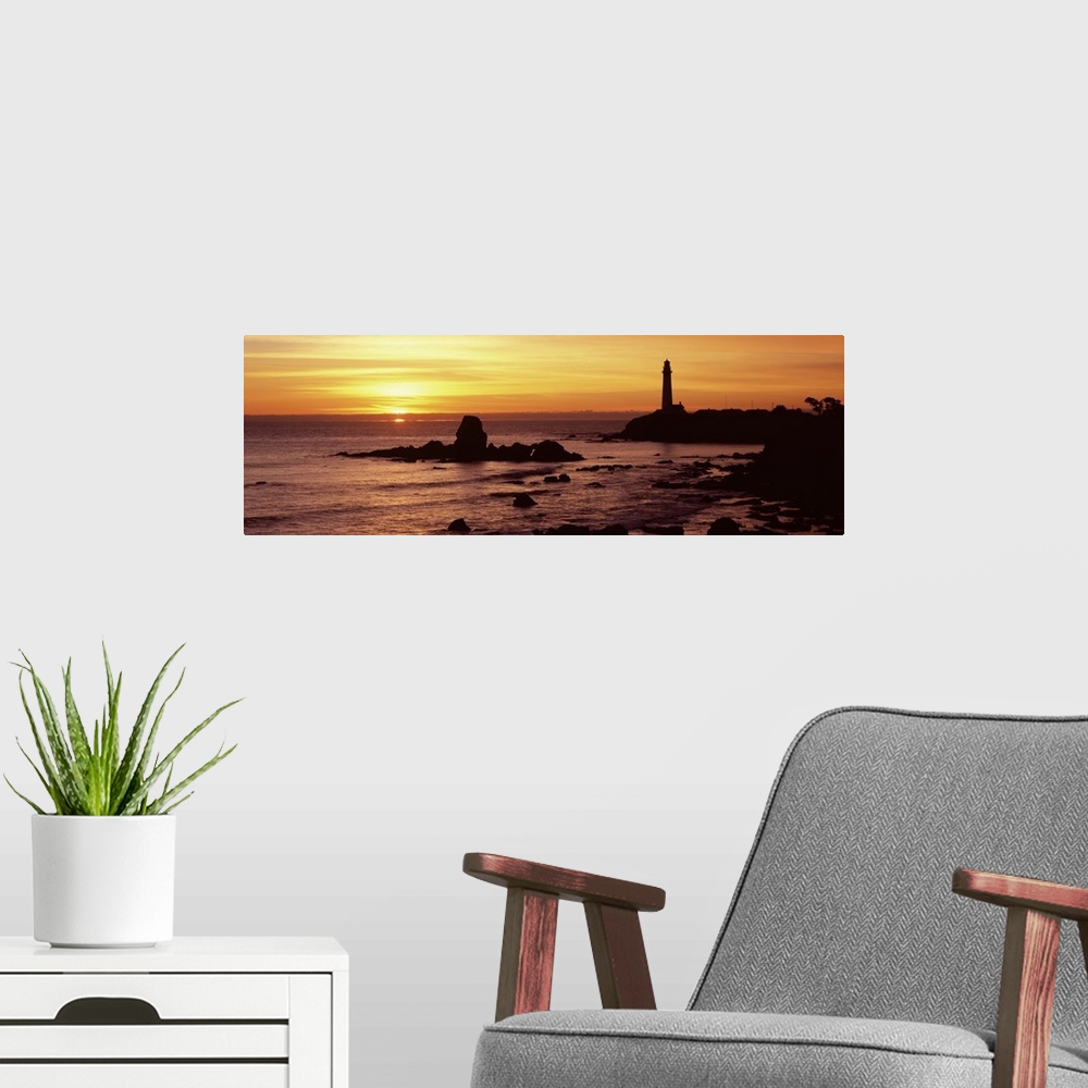 A modern room featuring A lighthouse and the cliffs surrounding it are silhouetted by the sunset over the Pacific ocean.