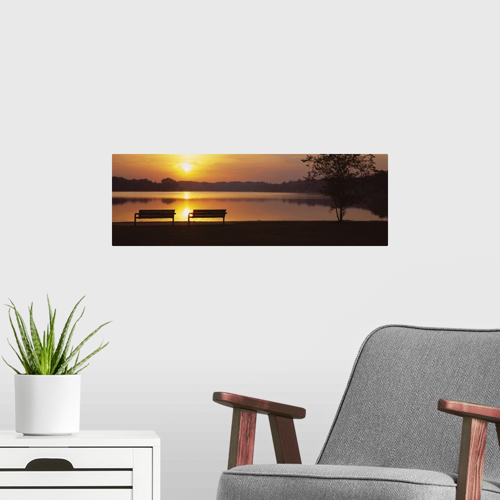 A modern room featuring Panoramic photograph of park benches near water's edge at sunset with forest silhouette in the di...