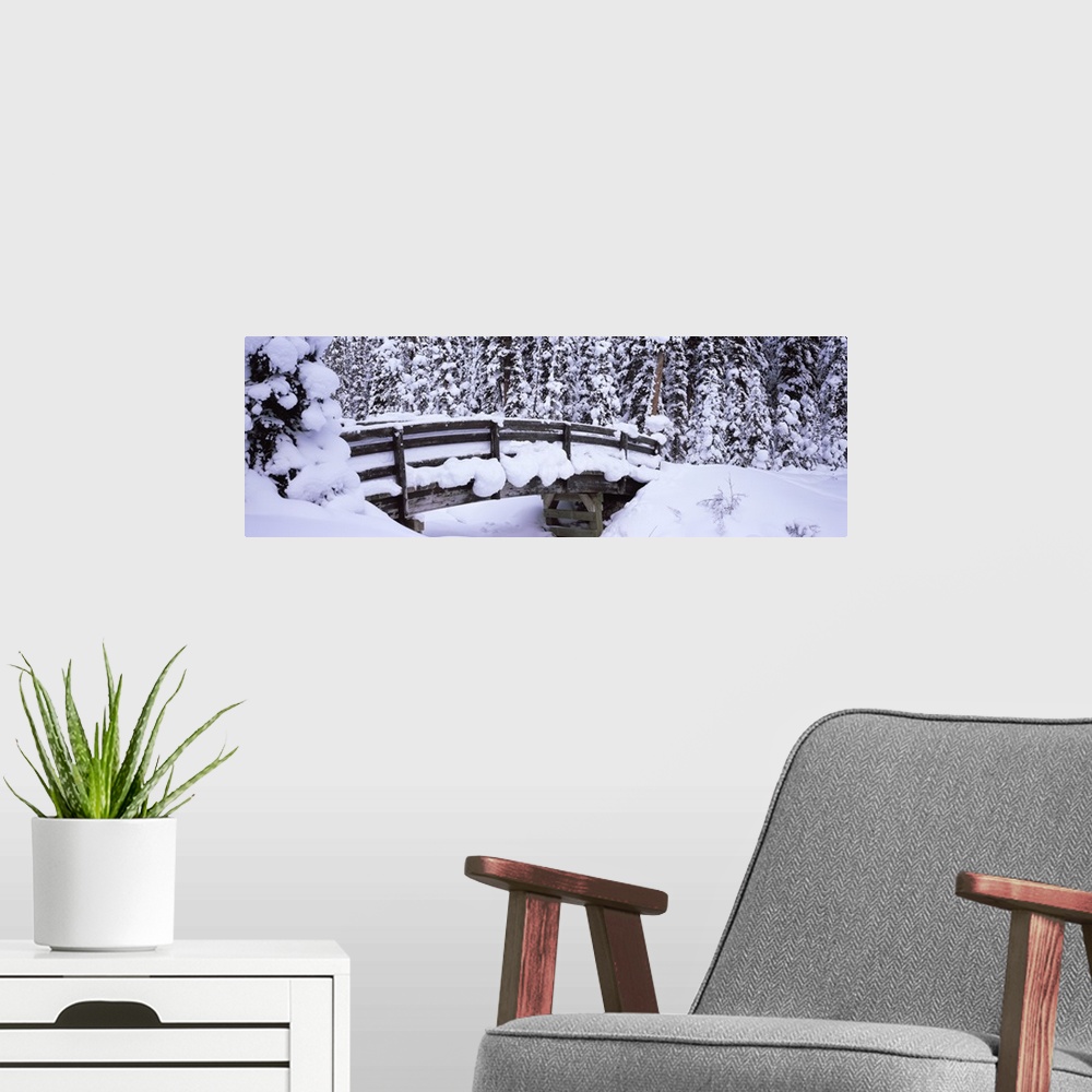A modern room featuring Long horizontal photo on canvas of a heavily snow covered bridge in the middle of a forest.