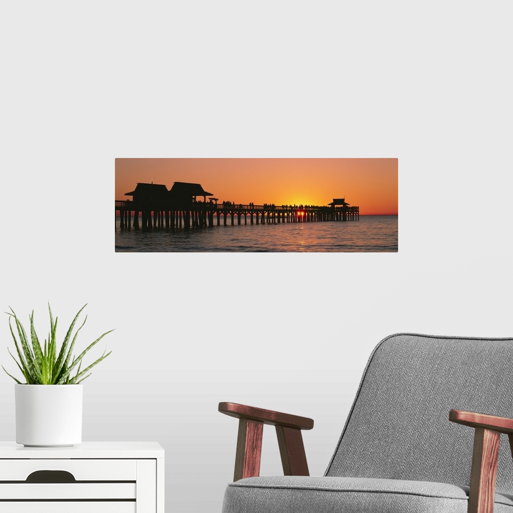 A modern room featuring Panoramic canvas photo art of a silhouetted pier at sunset on the ocean.