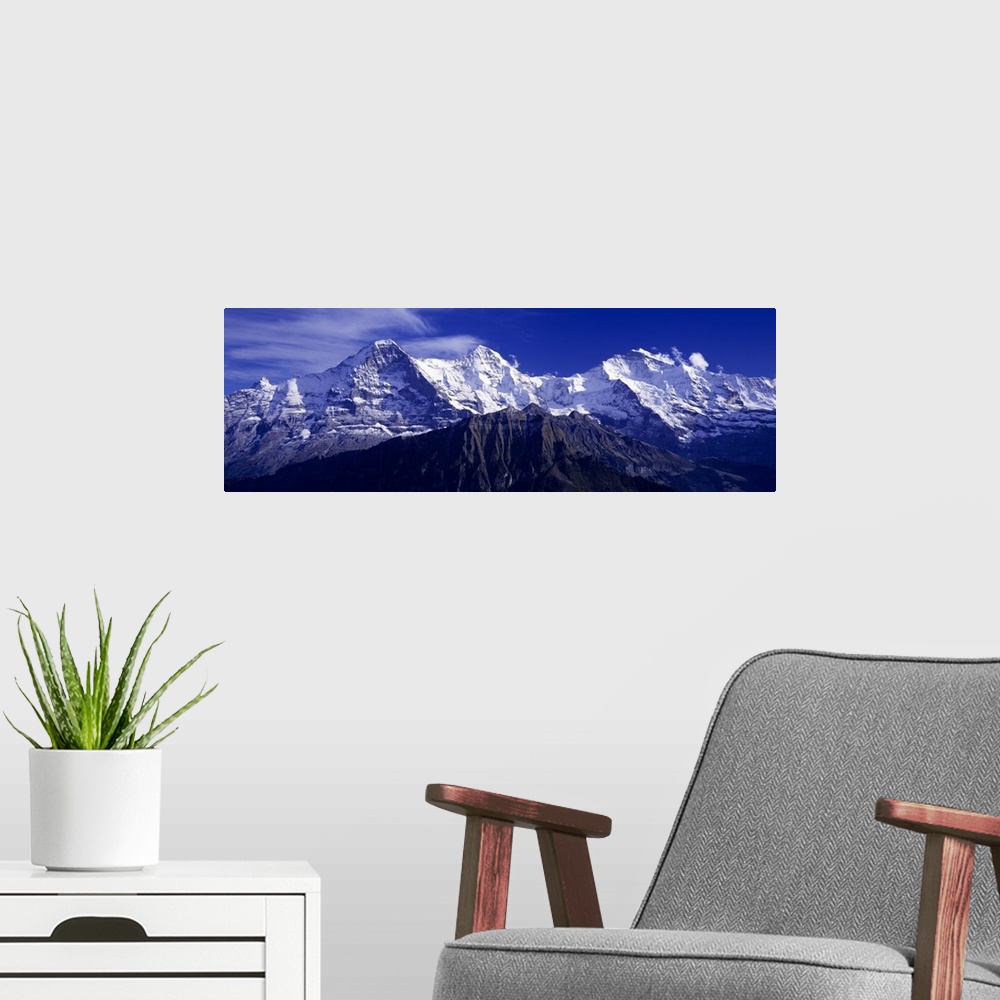 A modern room featuring Giant, landscape photograph of snow covered Swiss mountains against a deep blue sky in Berner, Ob...