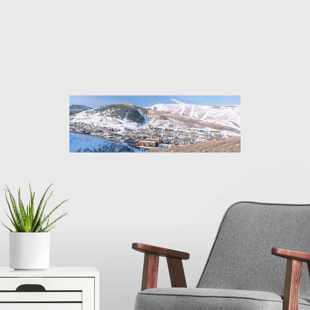 A modern room featuring Wide angle photograph on a large canvas of a distant town in a valley, surrounded by a snow cover...
