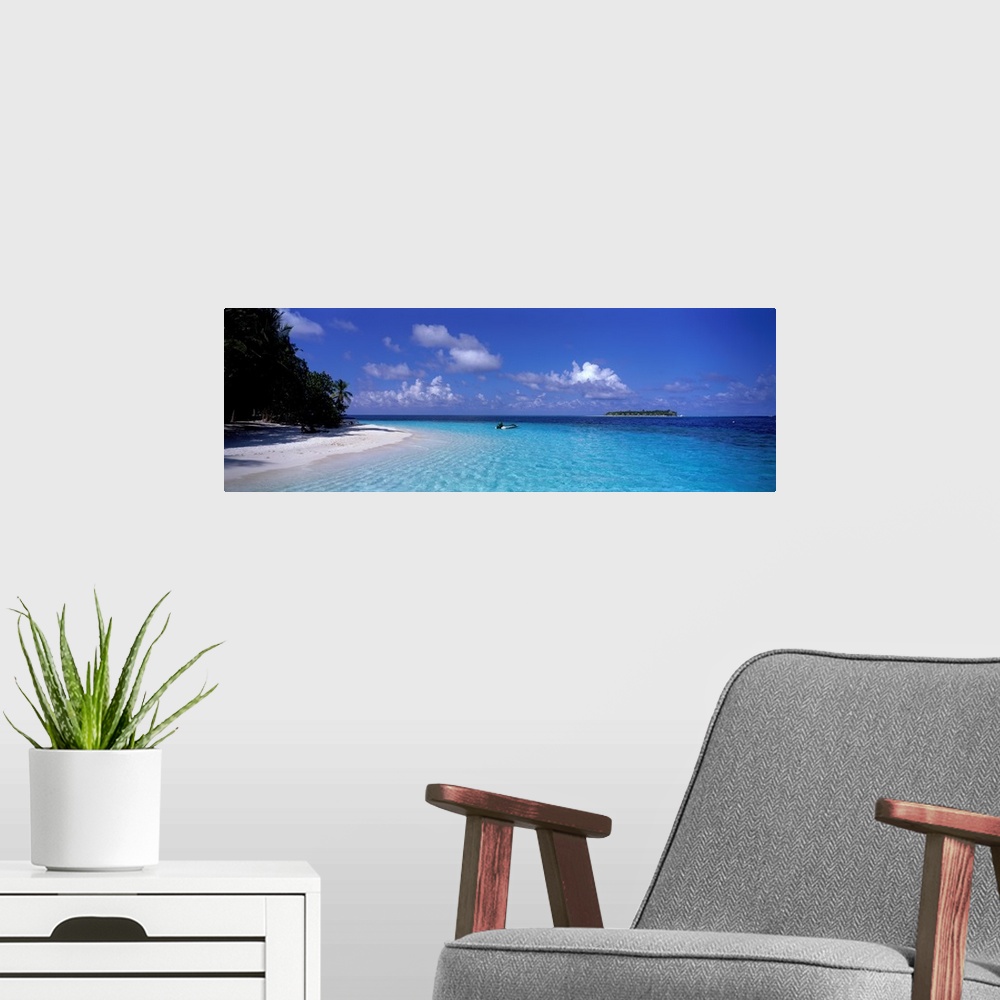 A modern room featuring This wide angle photograph is taken of clear ocean water that has a single boat sitting in it wit...