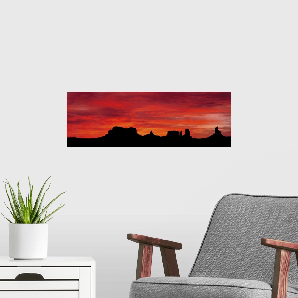 A modern room featuring Panoramic photograph of silhouettes of huge rock formations in the desert at sunset under a cloud...