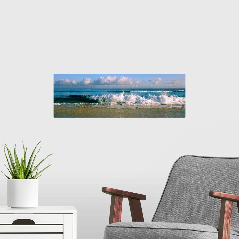 A modern room featuring Panoramic photograph of cloudy day at the beach with sea surf crashing onto the sand.