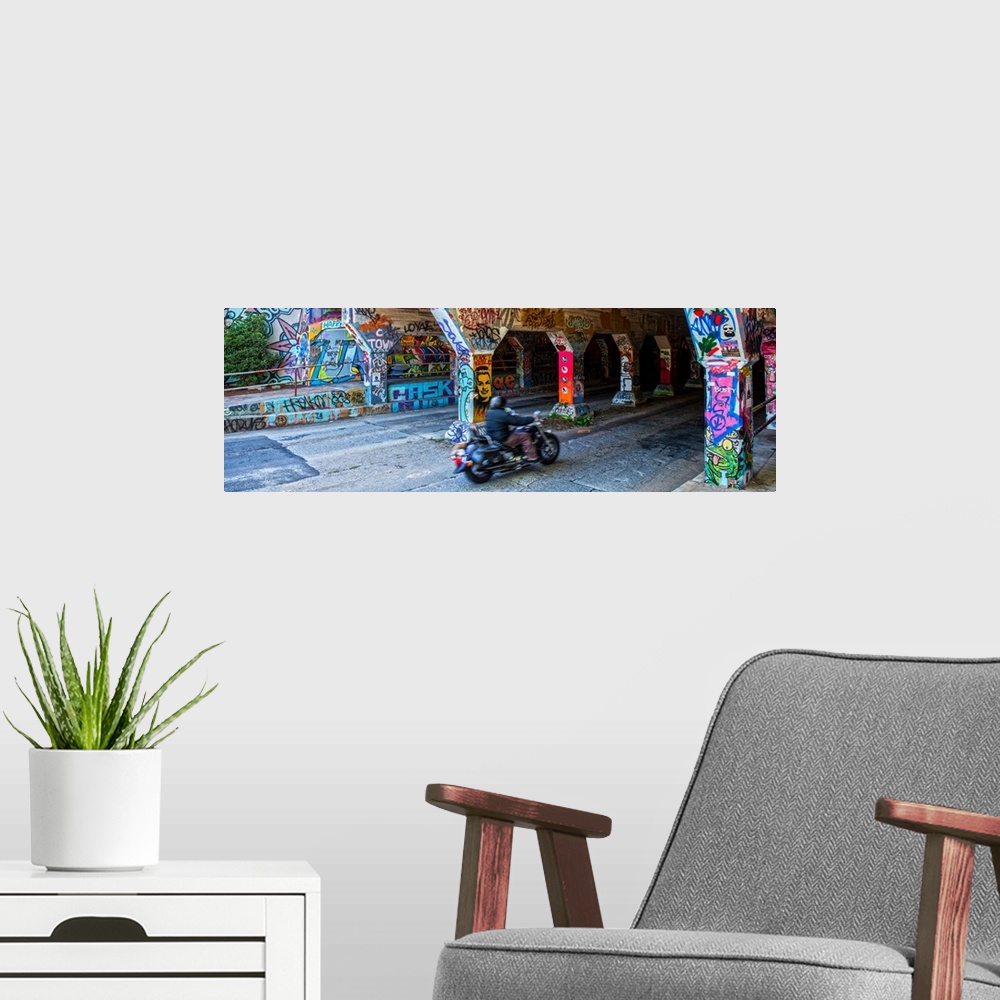 A modern room featuring A person on a motorcycle drives past columns and sidewalks covered in colorful graffiti at the en...