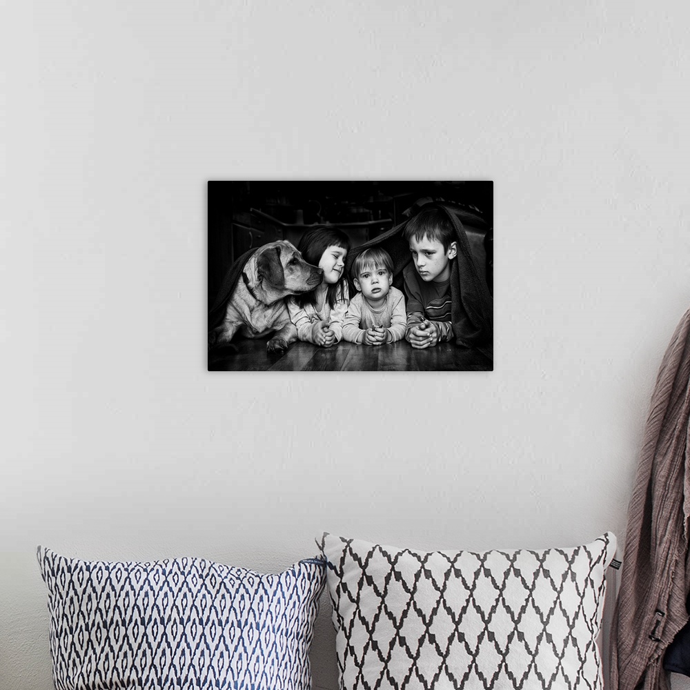 A bohemian room featuring Three siblings and their dog hiding together under a blanket.