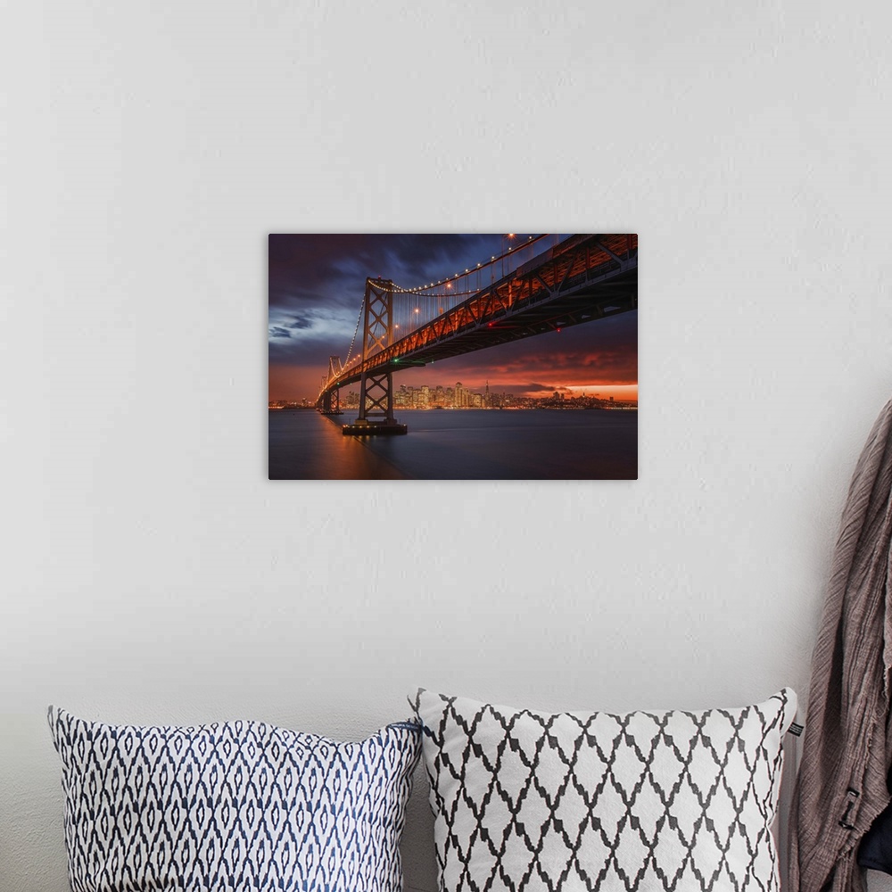 A bohemian room featuring The San Francisco bay bridge illuminated at night with a glowing sunset sky hanging over the city...