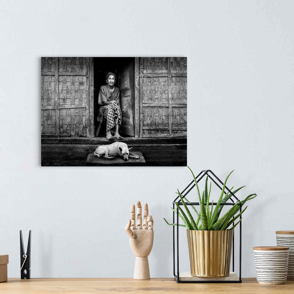 A bohemian room featuring An elderly woman sitting in her doorway with a dog at her feet, Bangli, Bali, Indonesia.