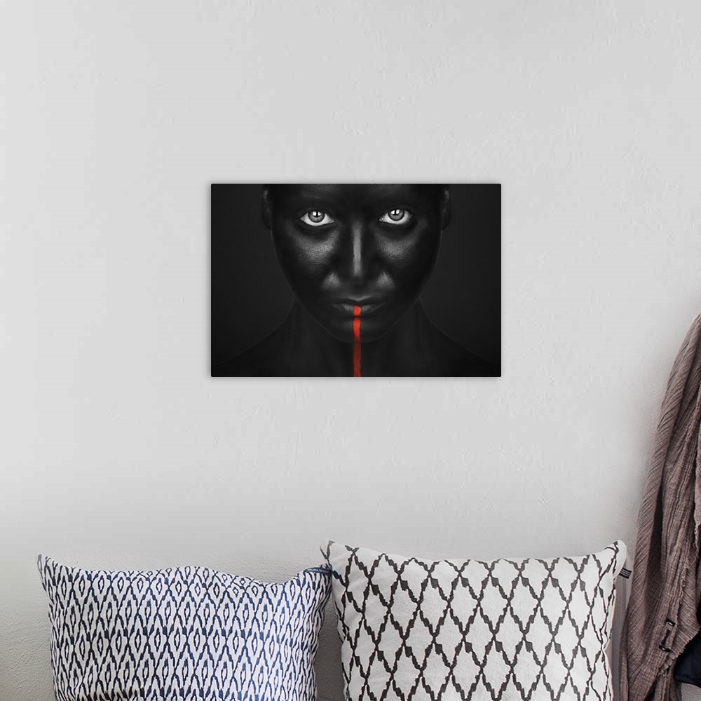 A bohemian room featuring A person with completely black bodypaint covering their face with a single red stripe running dow...
