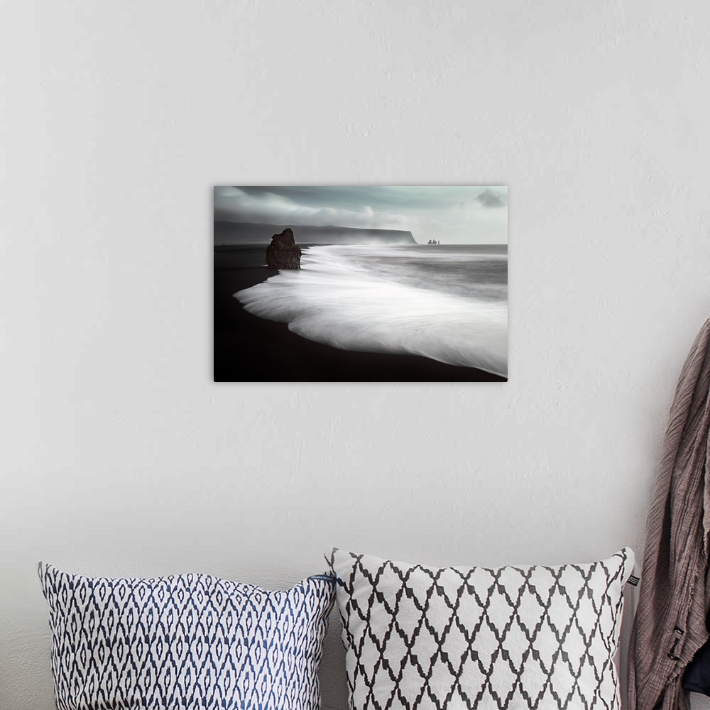 A bohemian room featuring Sea stacks on a black sand beach with rushing water on the coast of Iceland.