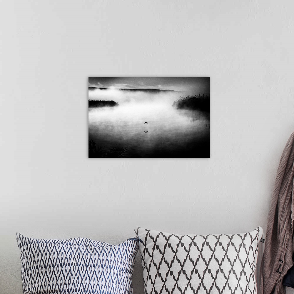 A bohemian room featuring Black and white image of a bird flying low over a foggy lake.