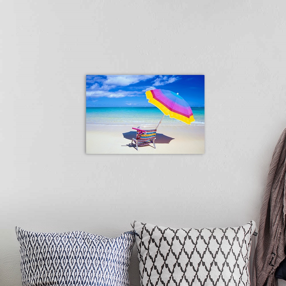 A bohemian room featuring A large photograph of a colorful beach chair and umbrella sitting solely on the sand close to the...