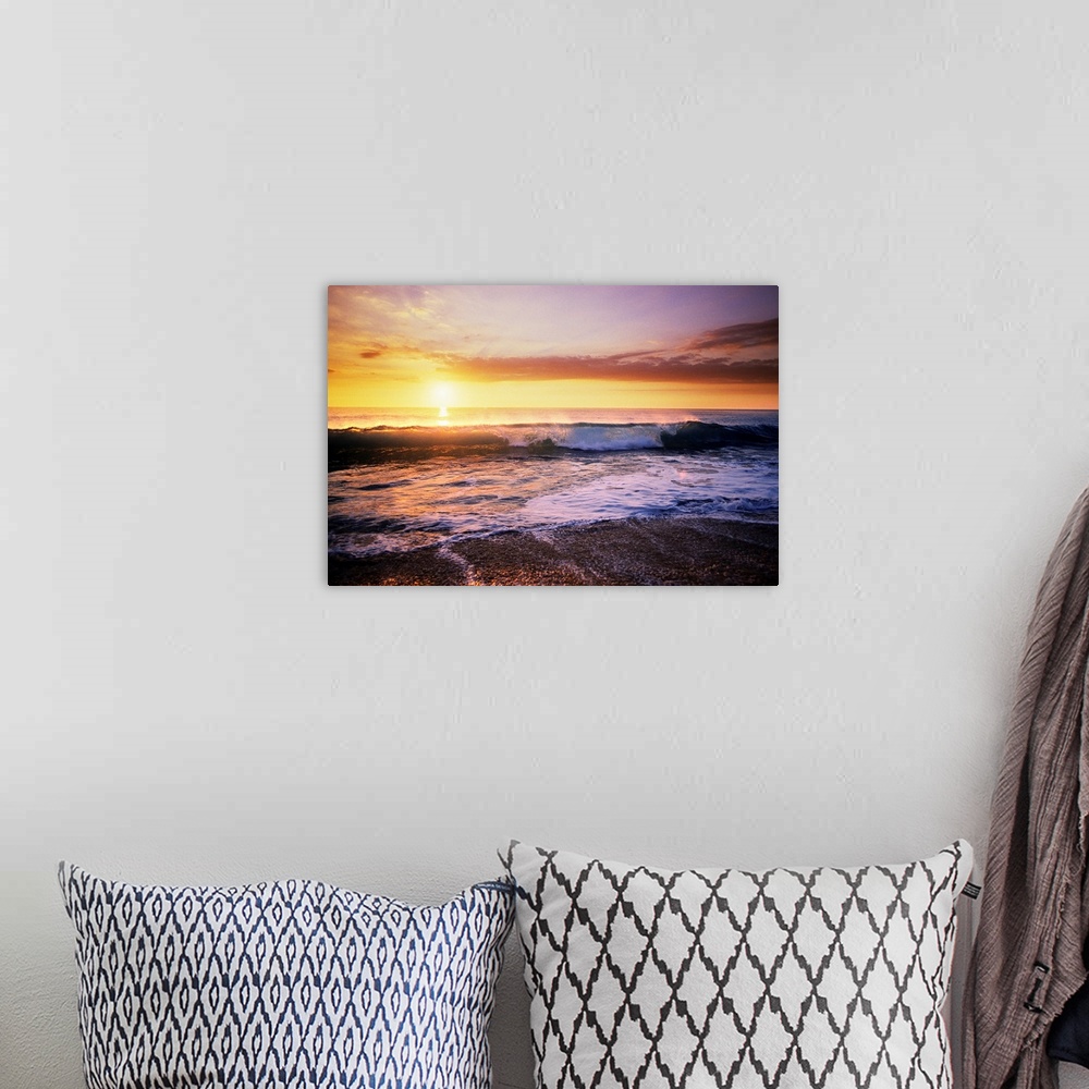 A bohemian room featuring The sun is setting in the distance over the ocean as a wave begins to crash near the edge of the ...