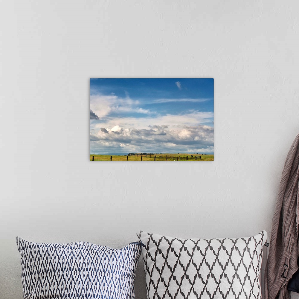 A bohemian room featuring Big blue sky with cumulus clouds fills most of image with slim view of grassland and fences of we...
