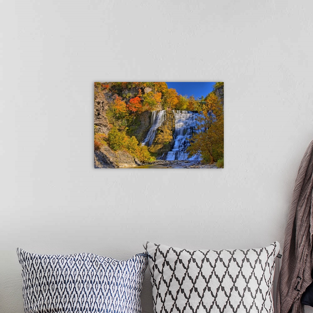 A bohemian room featuring This large piece is of a sizeable waterfall that is surrounded by autumn colored trees and foliage.