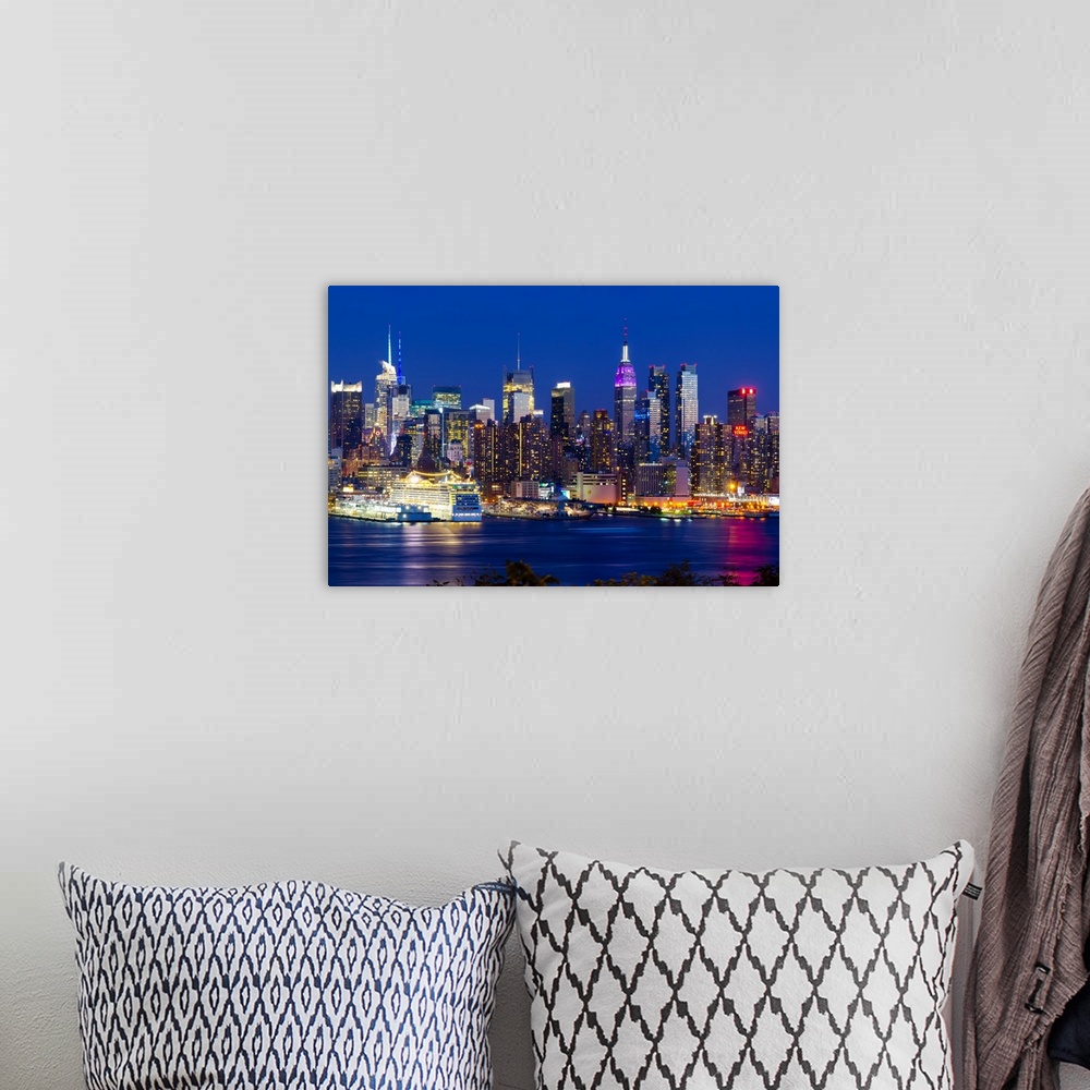 A bohemian room featuring Canvas print of the NYC cityscape lit up in colored lights along a waterfront.