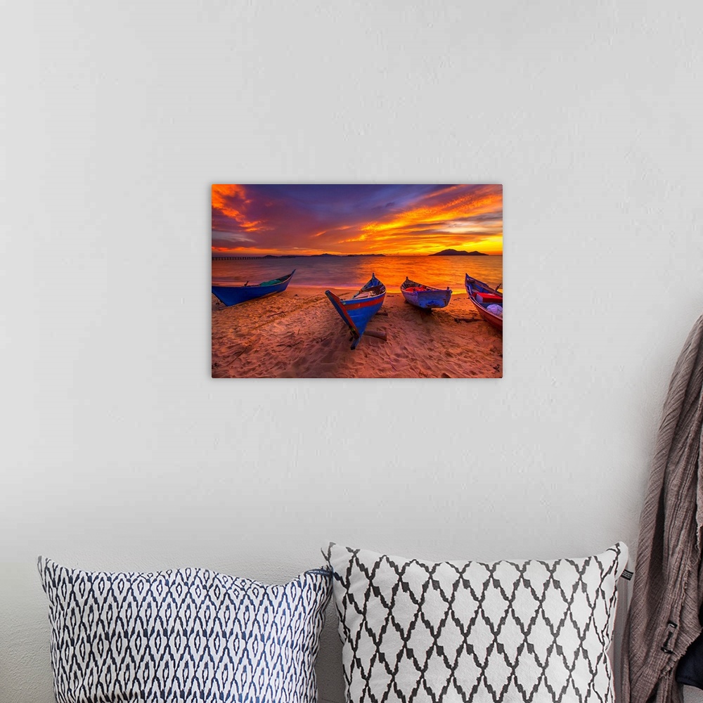A bohemian room featuring A row of small blue boats resting on the sandy beach with a brilliant sunrise.