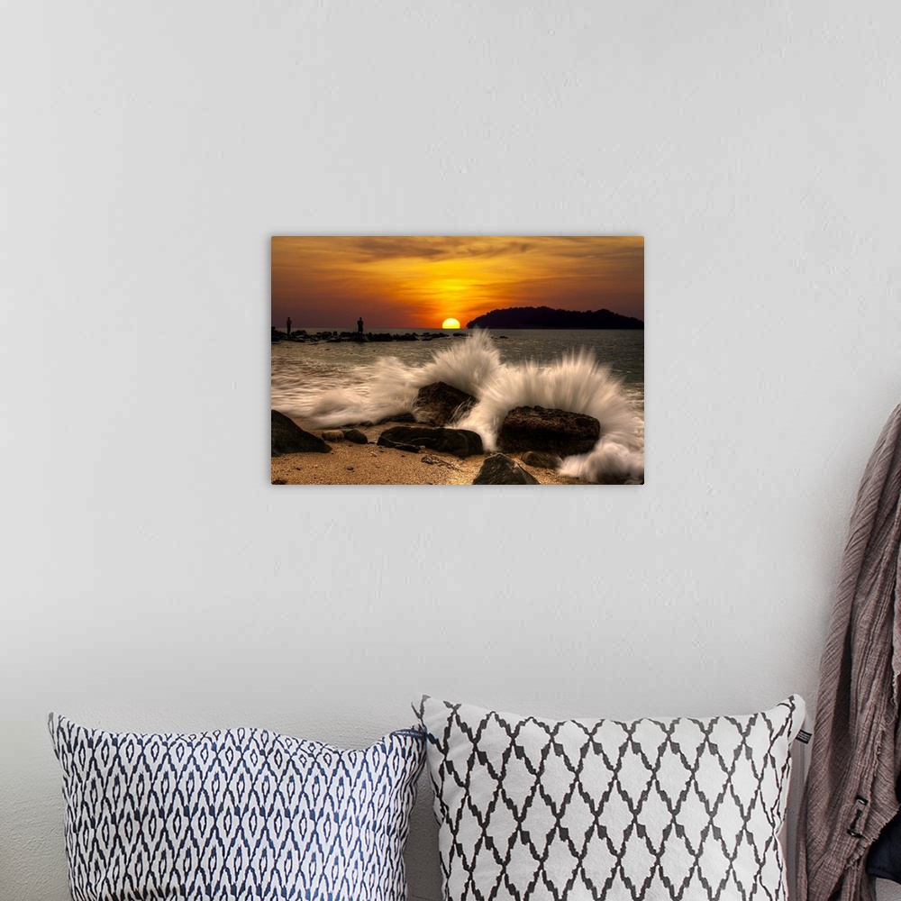 A bohemian room featuring Waves crashing onto rocks on the beach at sunset.