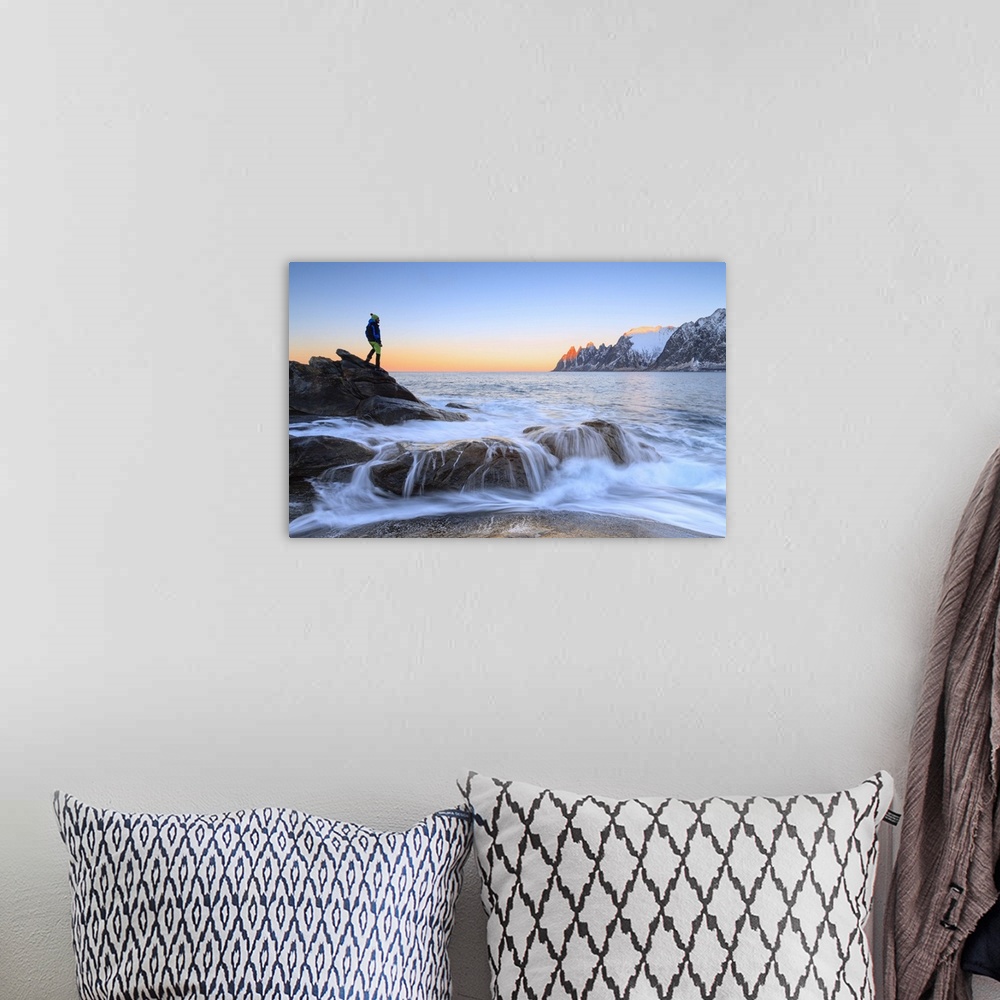 A bohemian room featuring Hiker admires the waves of the icy sea crashing on the rocky cliffs at dawn, Tungeneset, Senja, T...