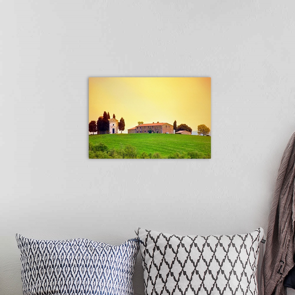 A bohemian room featuring Old traditional Tuscan farm buildings set on a green grass hill with a clear sunset sky.
