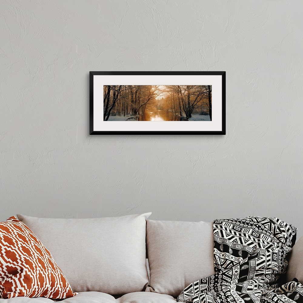 A bohemian room featuring Wall art of a snowy landscape full of trees is divided by a calm river backlit by warm sunlight.