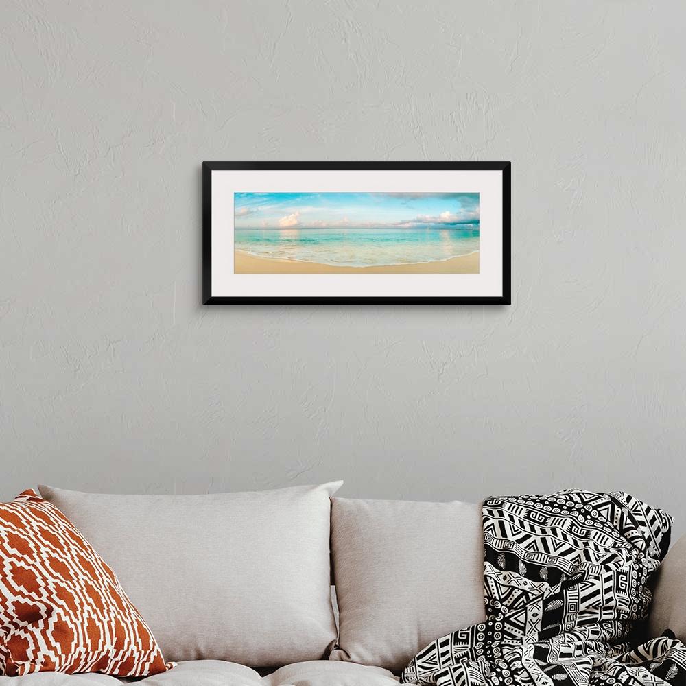 A bohemian room featuring A wide angle panoramic wall hanging of a calm tropical ocean, waves on the beach, and cumulus clo...