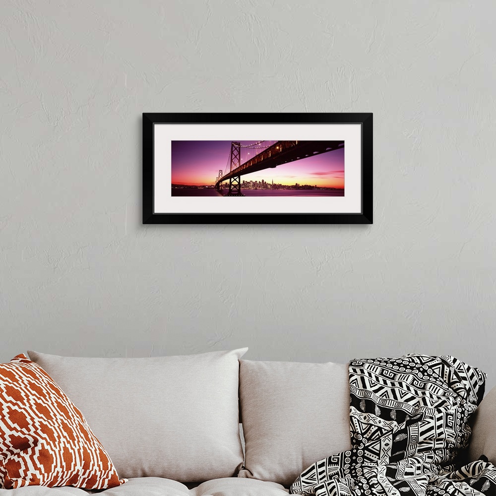 A bohemian room featuring Large panoramic photo print of a long bridge leading to a lit up city off in the distance at sunset.