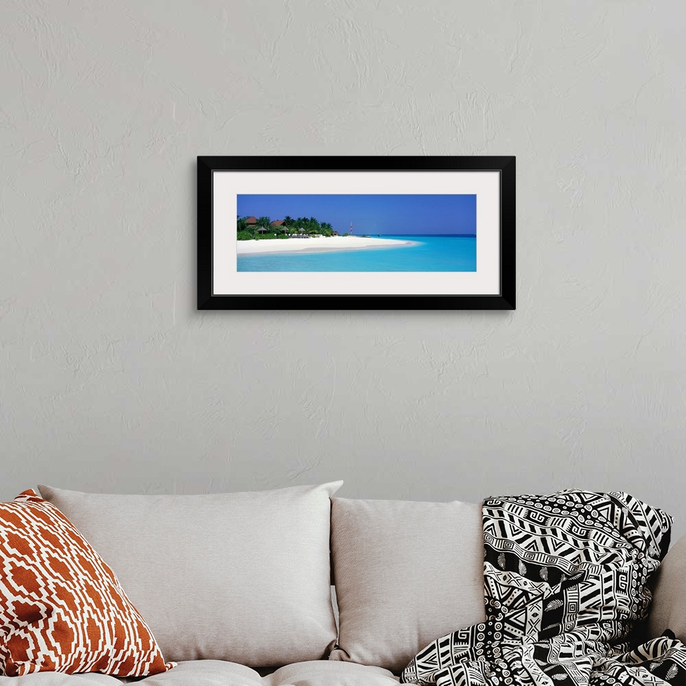 A bohemian room featuring This panoramic photograph is of a beach in Maldives with huts pushed back and surrounded by trees...