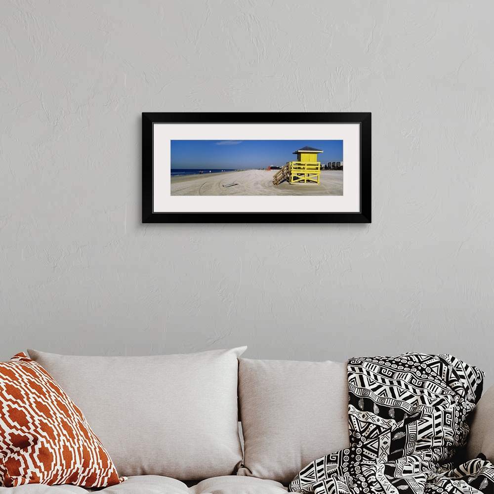 A bohemian room featuring A panoramic photograph of a mostly empty beach, there is a small shelter and abandoned surfboard ...