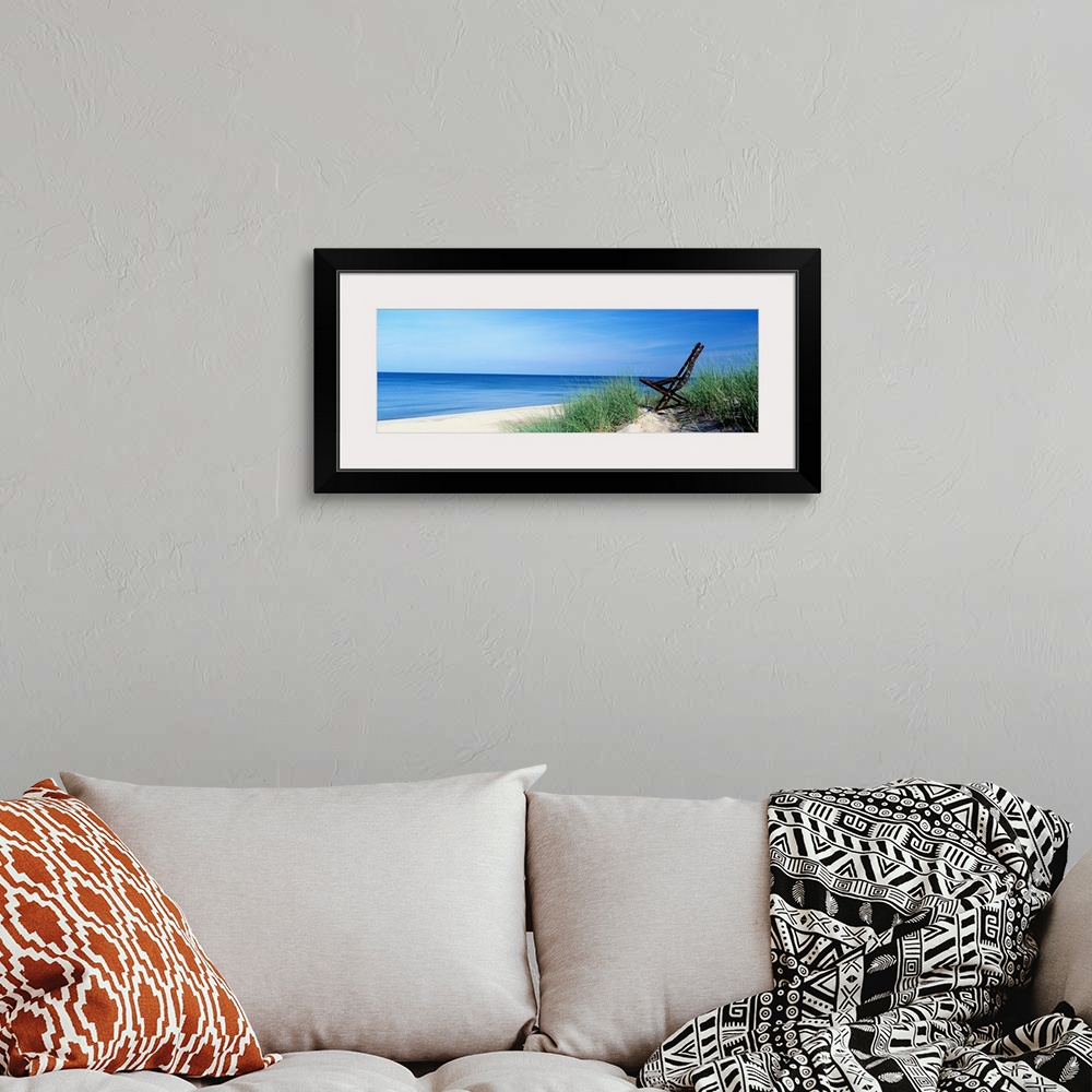 A bohemian room featuring This wall art is a panoramic landscape photograph of a sandy beach with a chair in the dunes over...