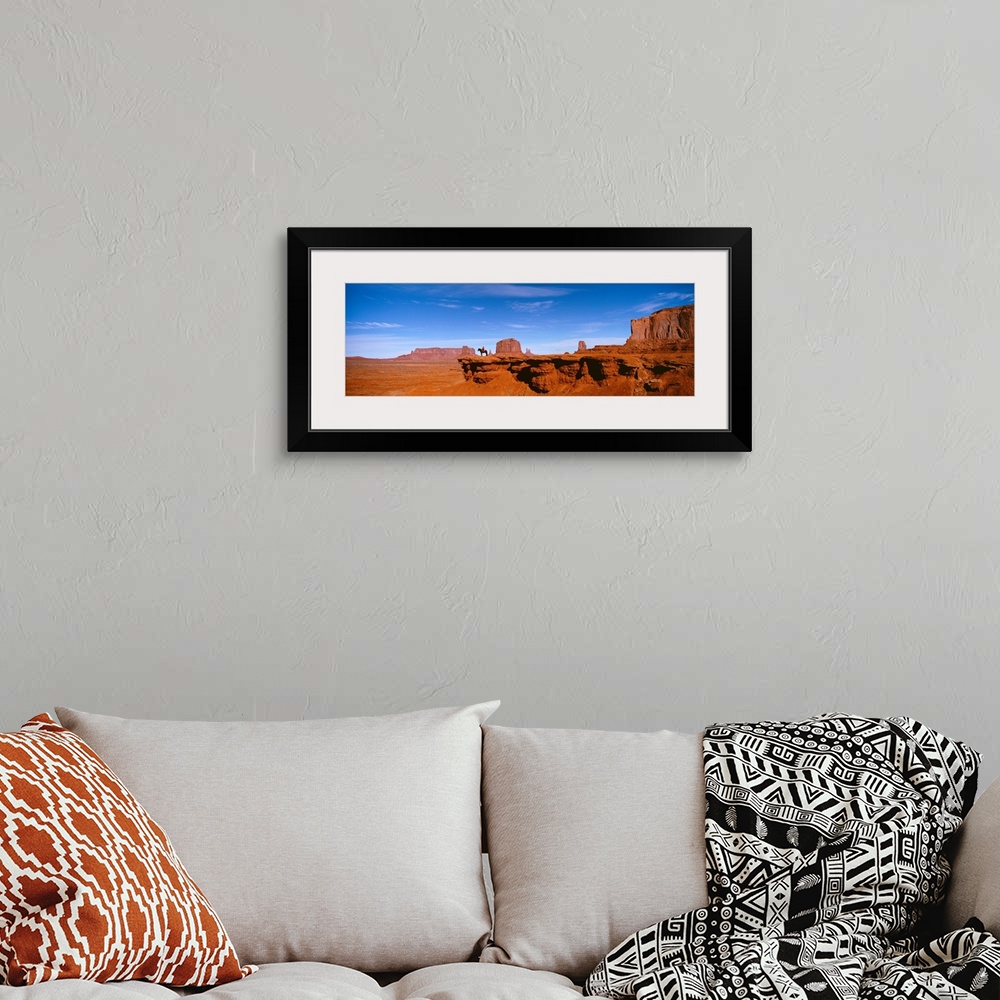 A bohemian room featuring A man on a horse at the edge of a cliff overlooking the arid desert of Monument Valley on a clear...