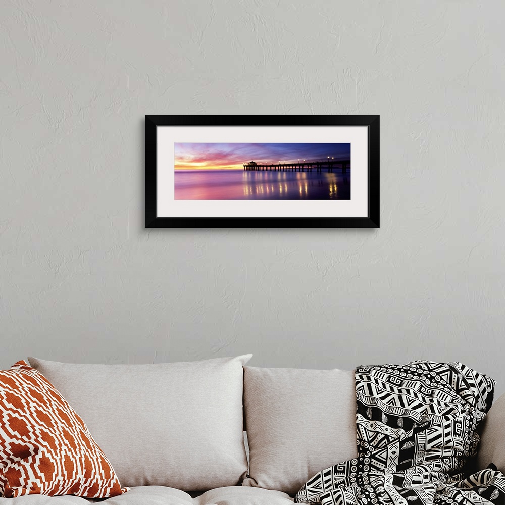 A bohemian room featuring Panoramic photograph of pier extending into ocean at sunset. The lights on the pier are reflected...