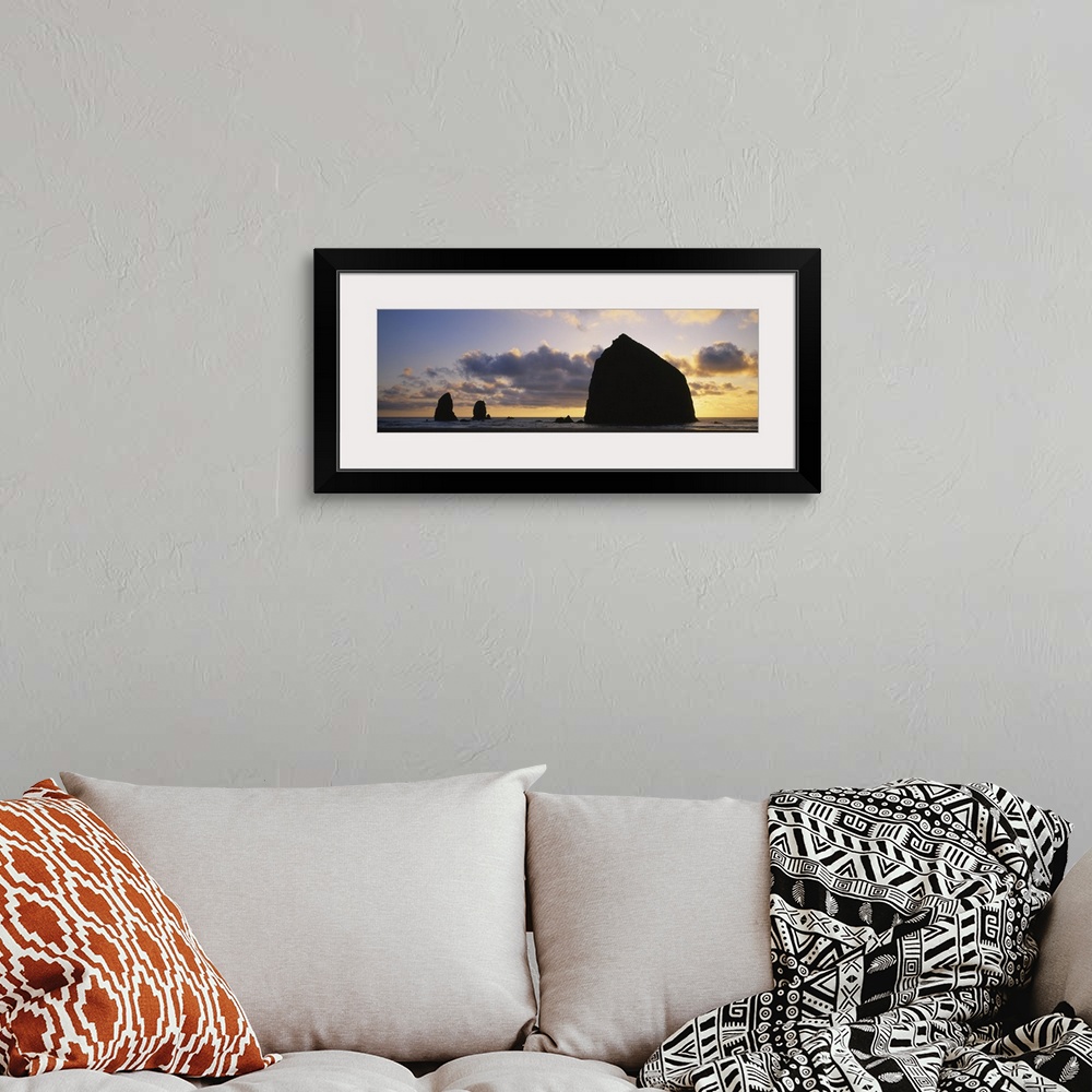 A bohemian room featuring Large panoramic piece of the sunset that silhouettes rock formations in the ocean.