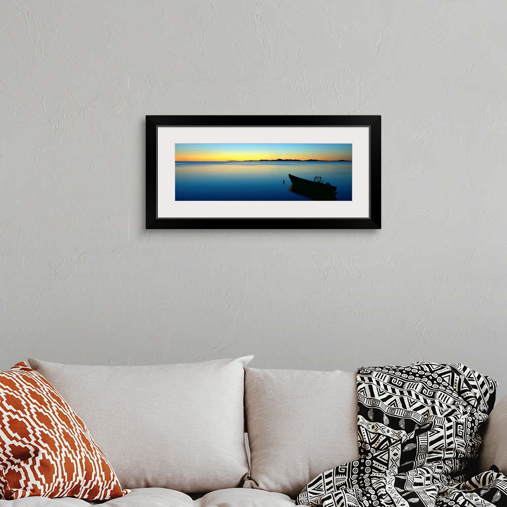 A bohemian room featuring Lonely boat resting on the calm ocean as the fading sun emits a golden glow on the horizon.
