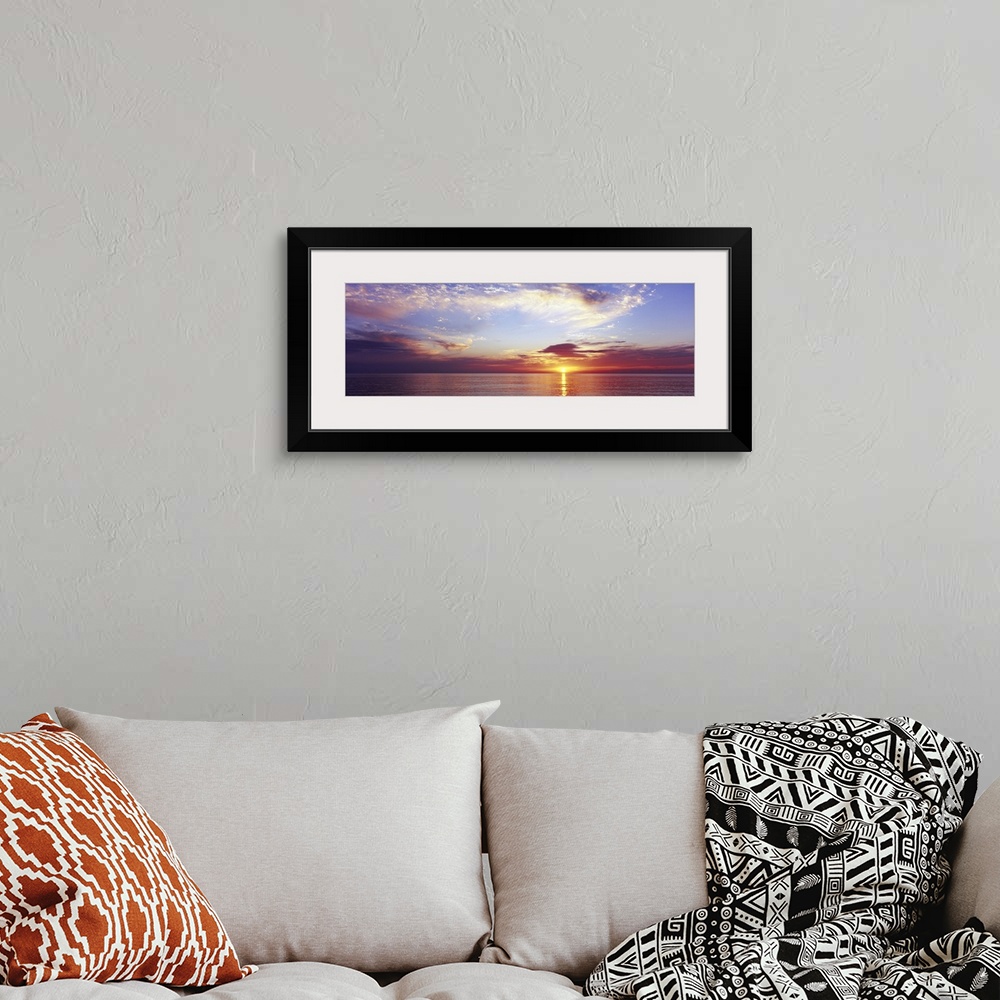 A bohemian room featuring Large panoramic photograph of a sunset over the ocean with a cloud filled sky.