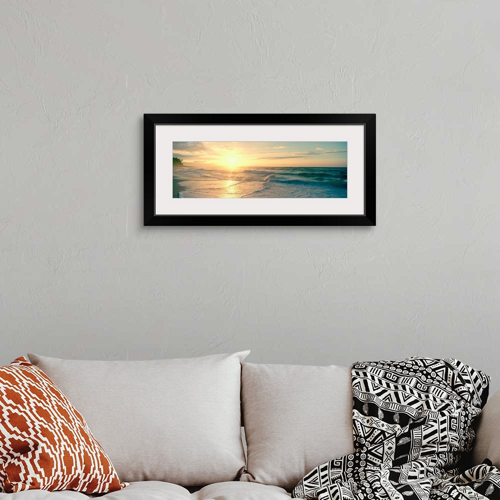 A bohemian room featuring Long panoramic print of an intense setting sun going down over the ocean with waves washing ashor...