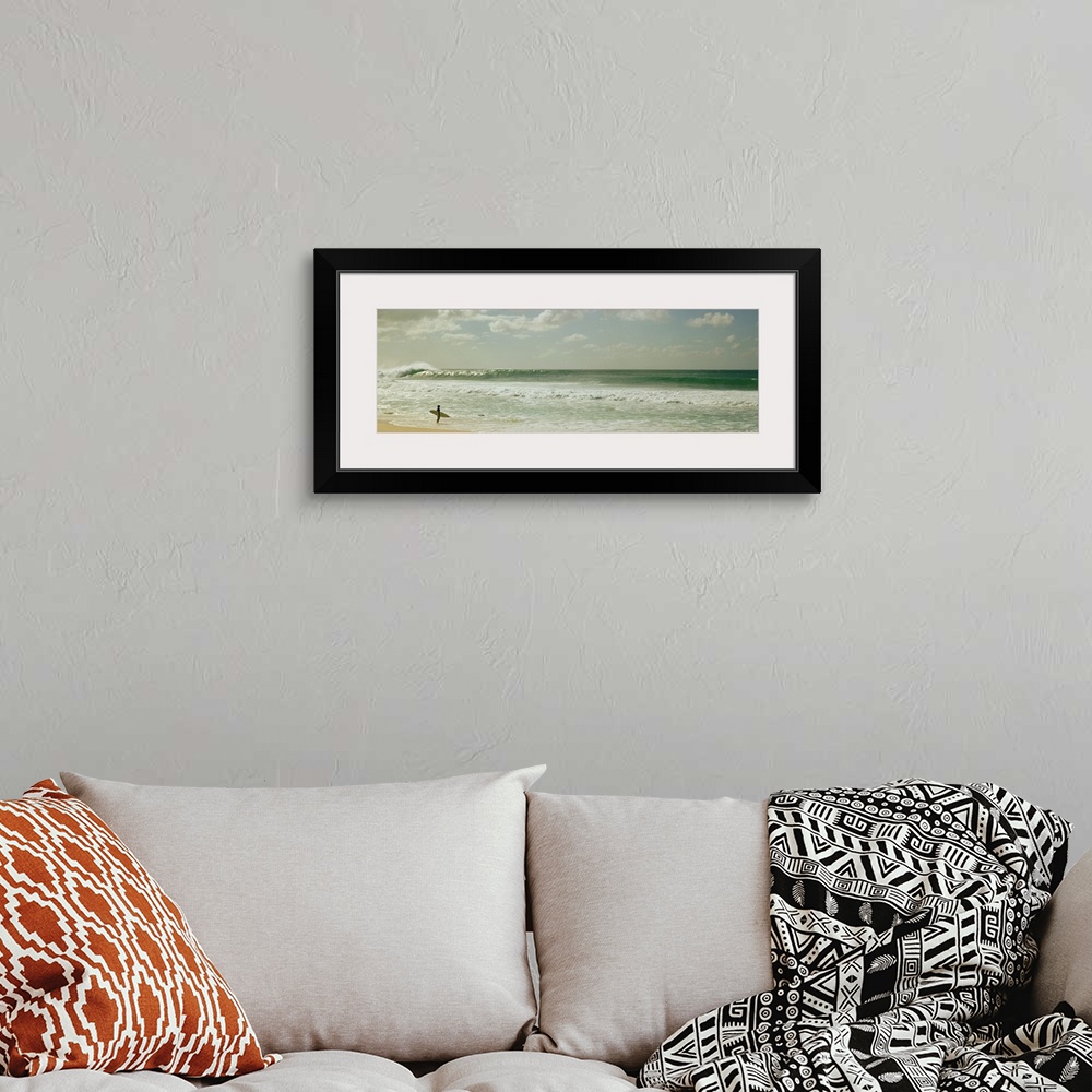A bohemian room featuring Panoramic image of a surfer standing where the ocean meets the beach shore looking at a big wave ...
